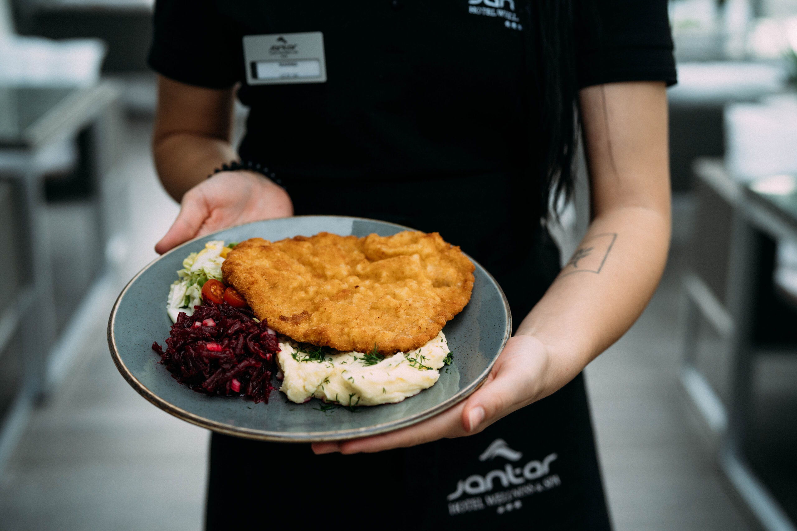Kotlet schabowy z ziemniakami, surówką z czerwonej kapusty i sałatką na białym talerzu.