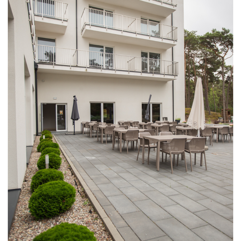 Zewnętrzny taras restauracyjny z krzesłami i stolikami przy budynku Hotelu Jantar